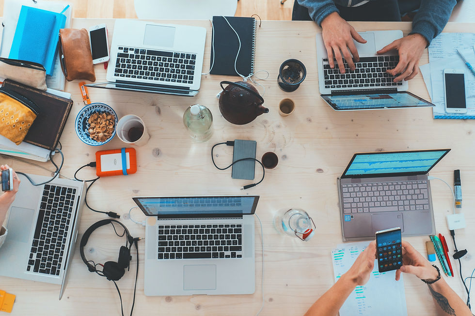 Five laptops two people using their cellphone and one person is using the laptop at the workplace..