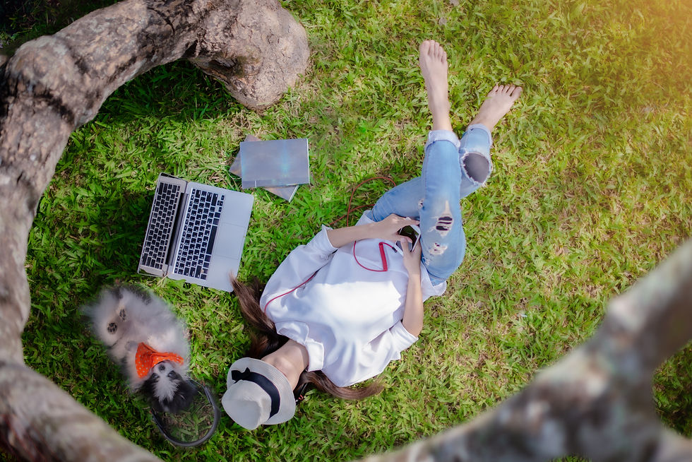 Woman lying in the ground relaxing while listening to music on  her smartphone  after working on her laptop. 