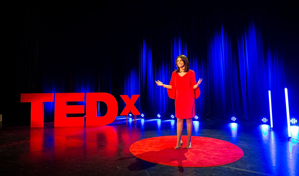 woman in red dress speaking on stage at TEDx