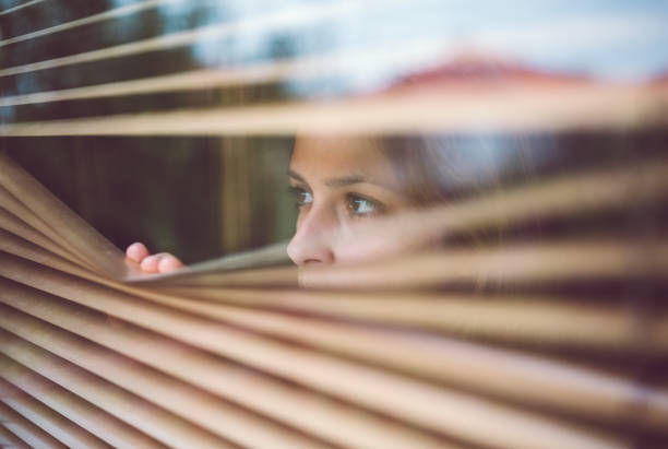 Woman at home looking through the persiennes.