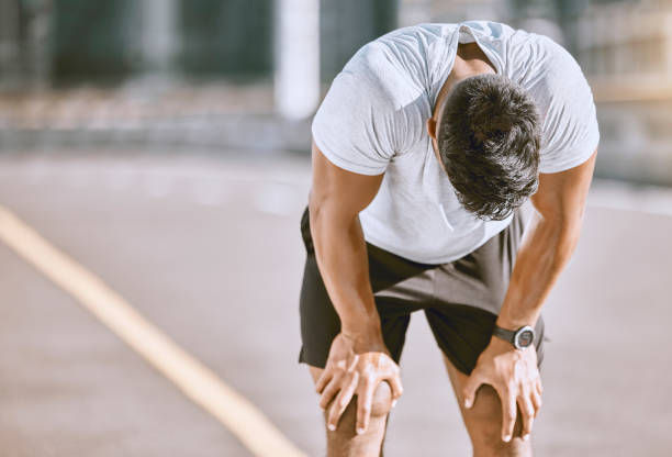 A photo of tired man resting after fitness run, taking a break from cardio training and doing wellness exercise on the road.