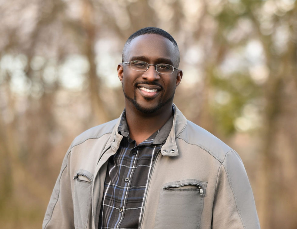 Shot of a man smiling at the camera with trees on the background.