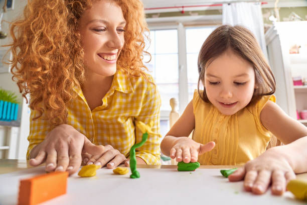 Mother and daughter sitting at table molding using modeling clay laughing cheerful