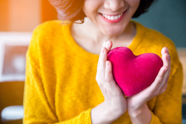 woman hands in yellow sweater holding pink heart. 