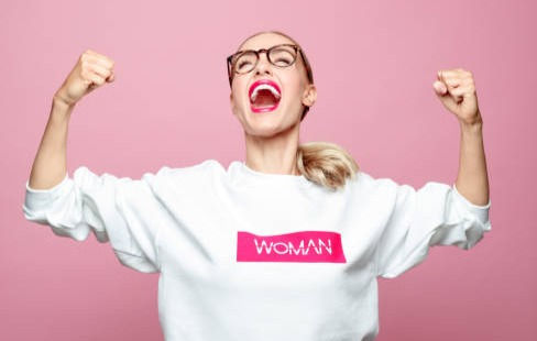 Successful woman clenching fists. Beautiful strong female is screaming against pink background.