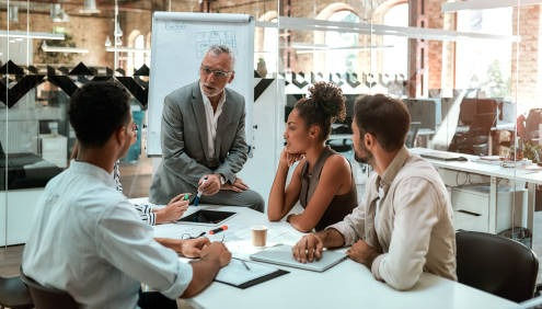 Mature businessman talking about something with his young colleagues while sitting together at the office table 