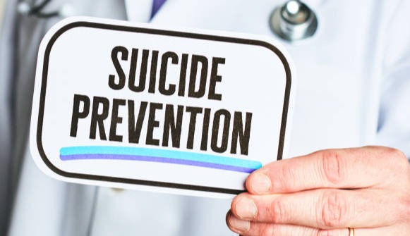 Unidentifiable male in a lab coat holding a medical sign: Suicide Prevention