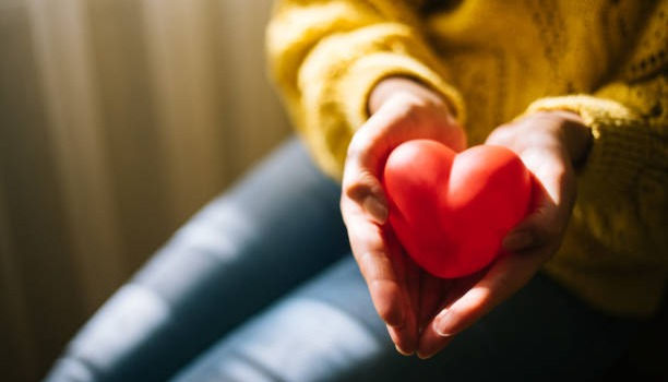 Woman in yellow sweater holding red heart.
