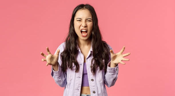 Young girl losing temper, screaming furious and angry in pink background.