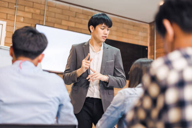 Young  male coach or speaker make flip chart presentation to businesspeople at meeting in office. 