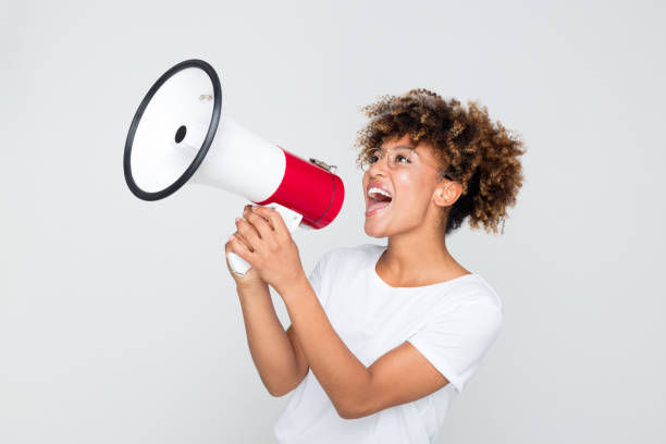 Woman yelling into a megaphone on grey background.