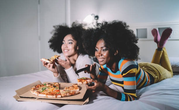 Girlfriends eating pizza in bed and watching TV