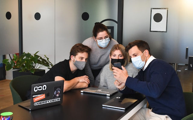 one co-worker showing other team members something on the phone at the office