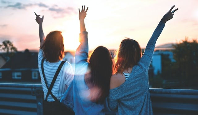 Photo of three woman lifting there hands on a beautiful sunset